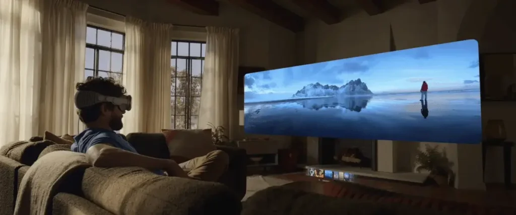 Man wearing Apple Vision pro watches a panoramic landscape video on a large screen in a living room.
